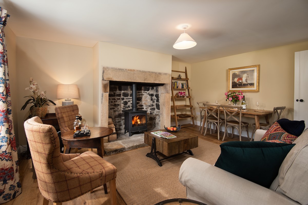 Aydon Castle Cottage - sitting room with large fireplace and dining space for four guests