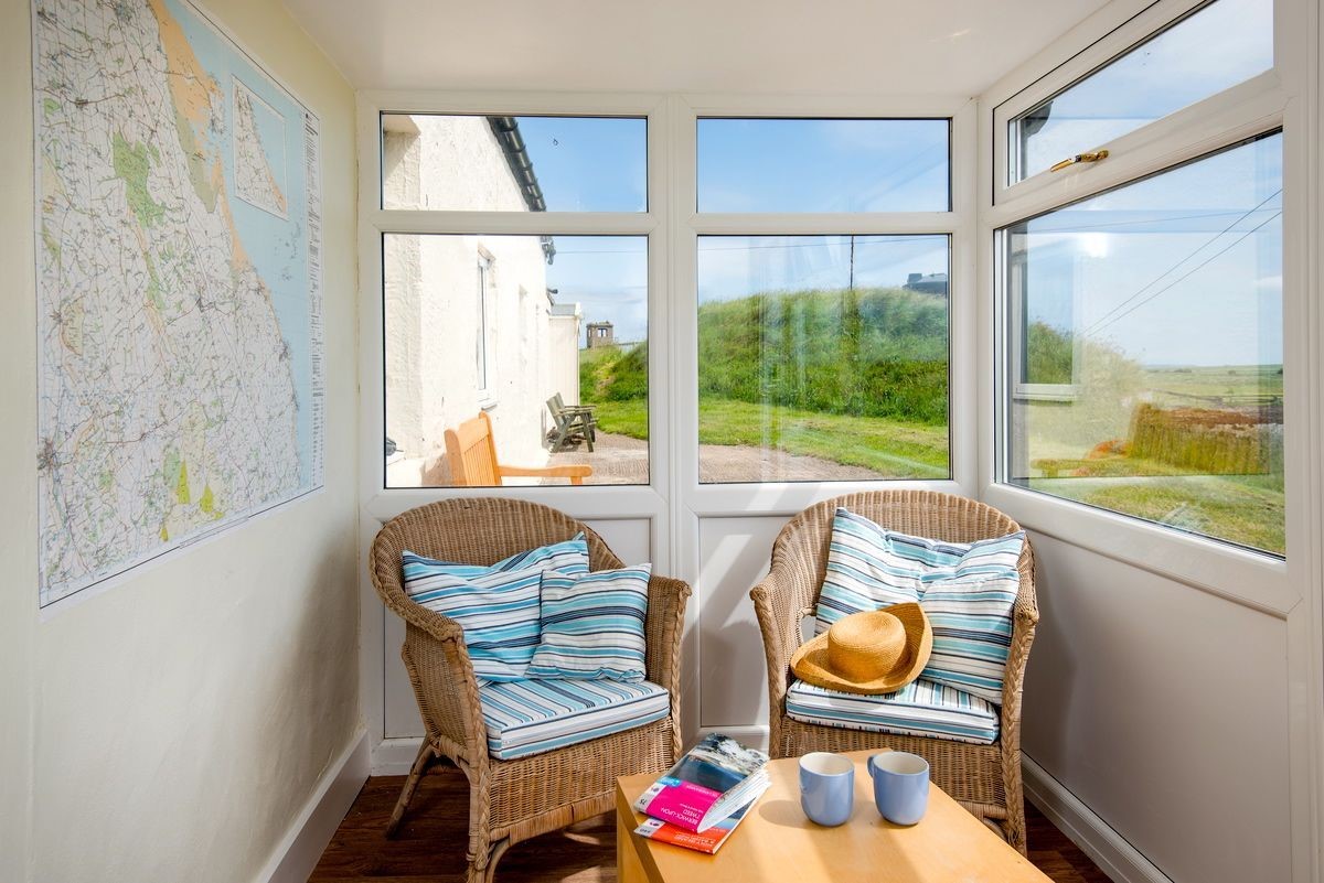 Beachcomber Cottage - the access porch with wicker chairs and map of local area