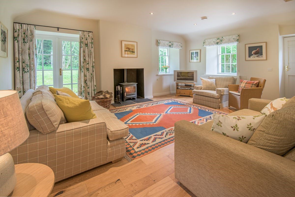 Gardener's Cottage - spacious sitting room with two sofas, armchairs, wood burning stove and French doors
