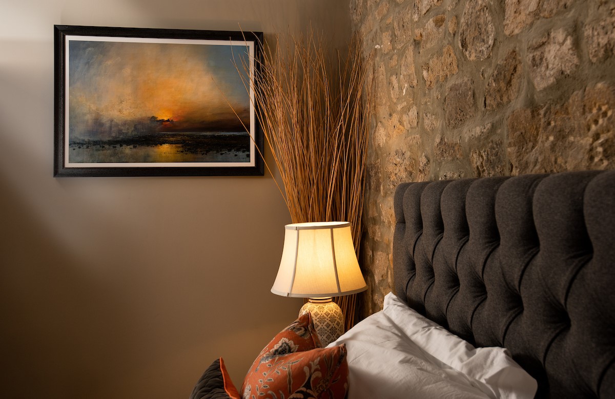 Coach House - bedroom one with beautiful artwork, exposed stone and decorative details