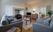 Chaffinch Cottage - sitting room with sofa, armchair, dining space, TV and wood burning stove