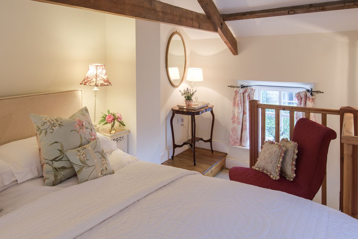 A mezzanine level bedroom with wooden beams and pretty decor in a country cottage in Northumberland.