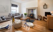 Chaffinch Cottage - sitting room with sofa, armchair, wood burning stove and dining area seating four guests