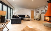 Coledale Stables - open-plan sitting room with large corner sofa, armchair and wood burning stove